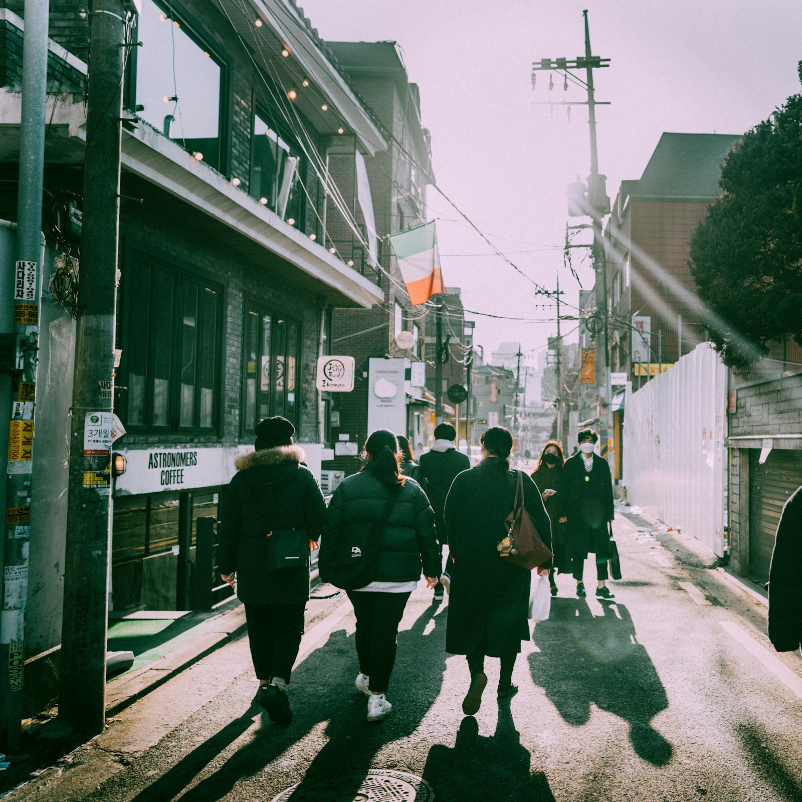 Personas recorren una calle urbana iluminada por el sol entre fachadas y sombras.